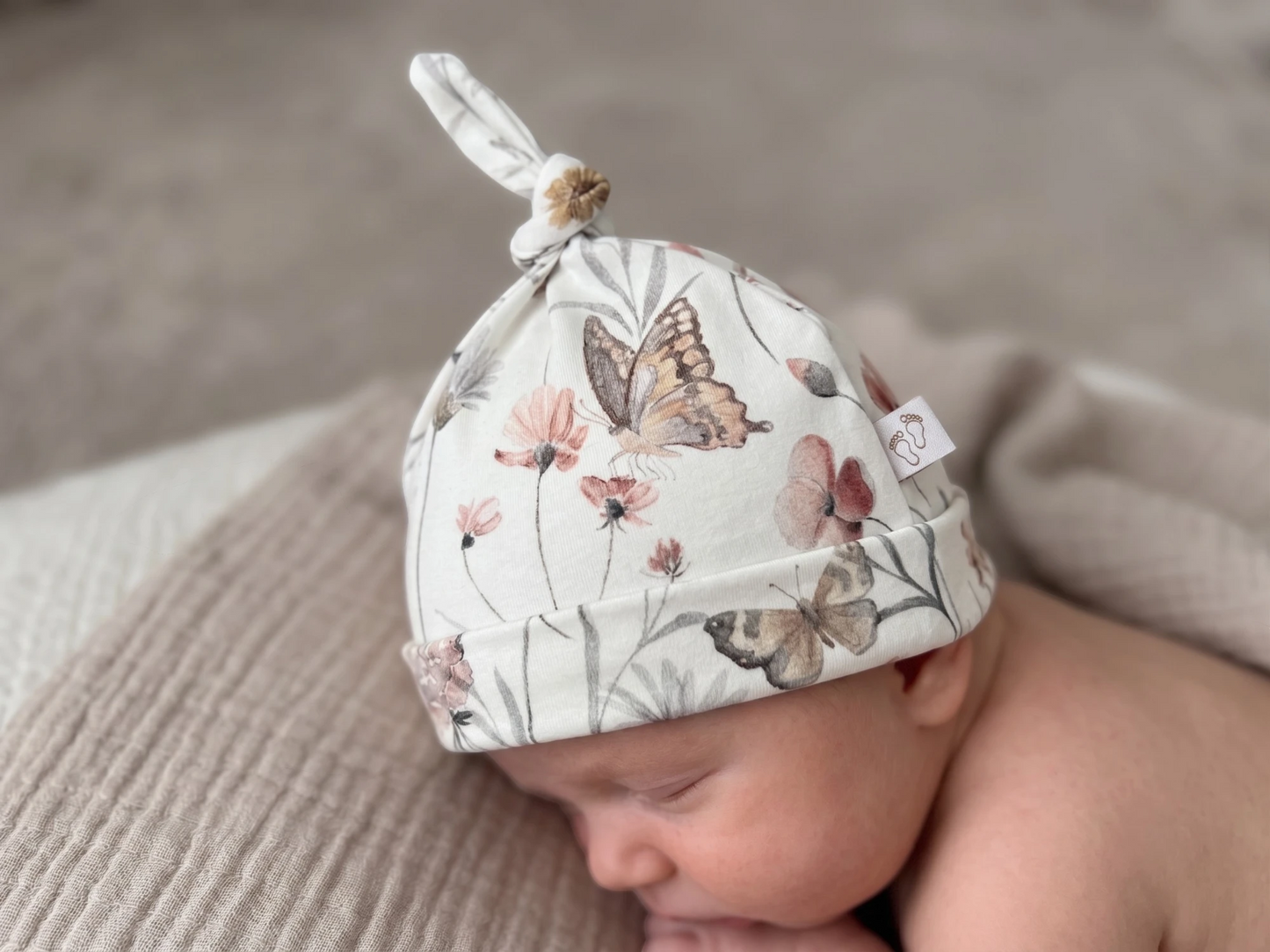 Baby met babymutsje in bloemen en vlinders print in een zachte neutrale setting