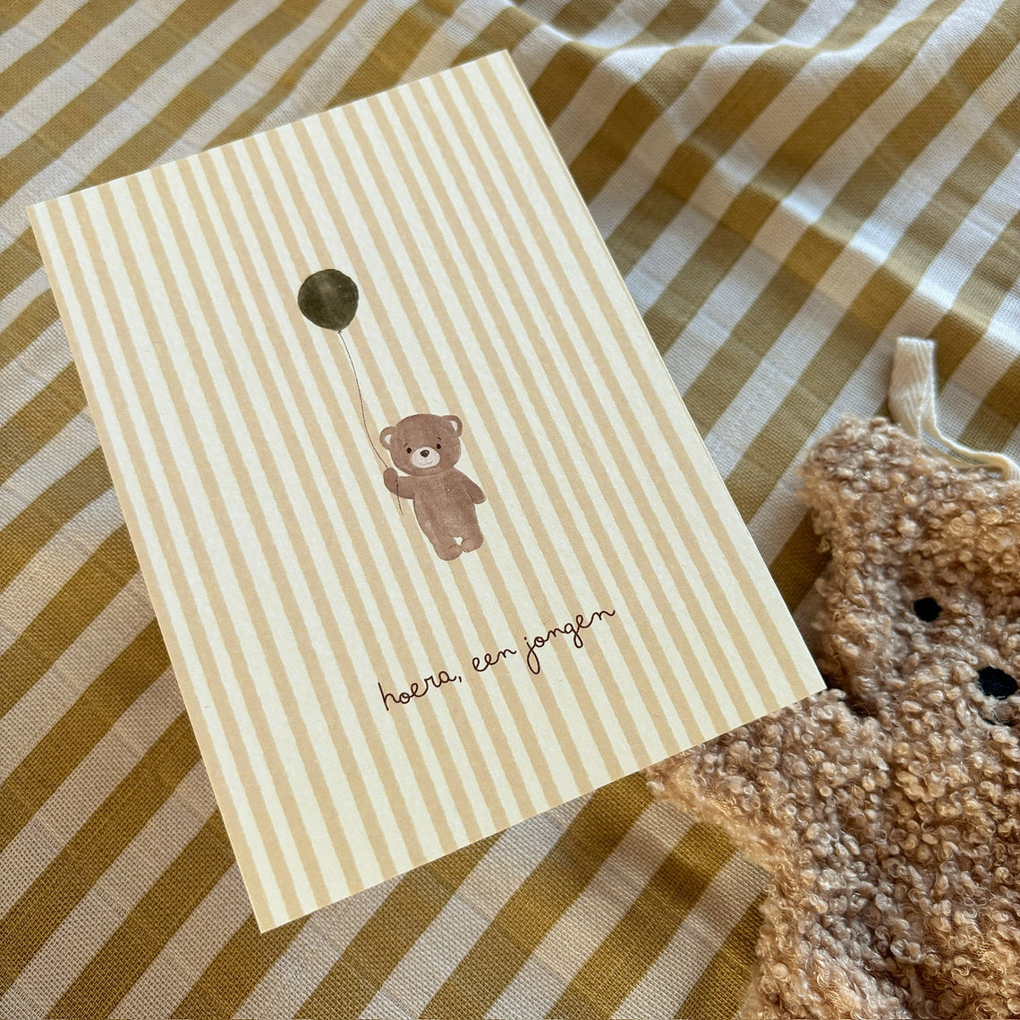 Beige gestreepte ansichtkaart voor de geboorte van een jongen met beertje, ballon en tekst Hoera, een jongen.