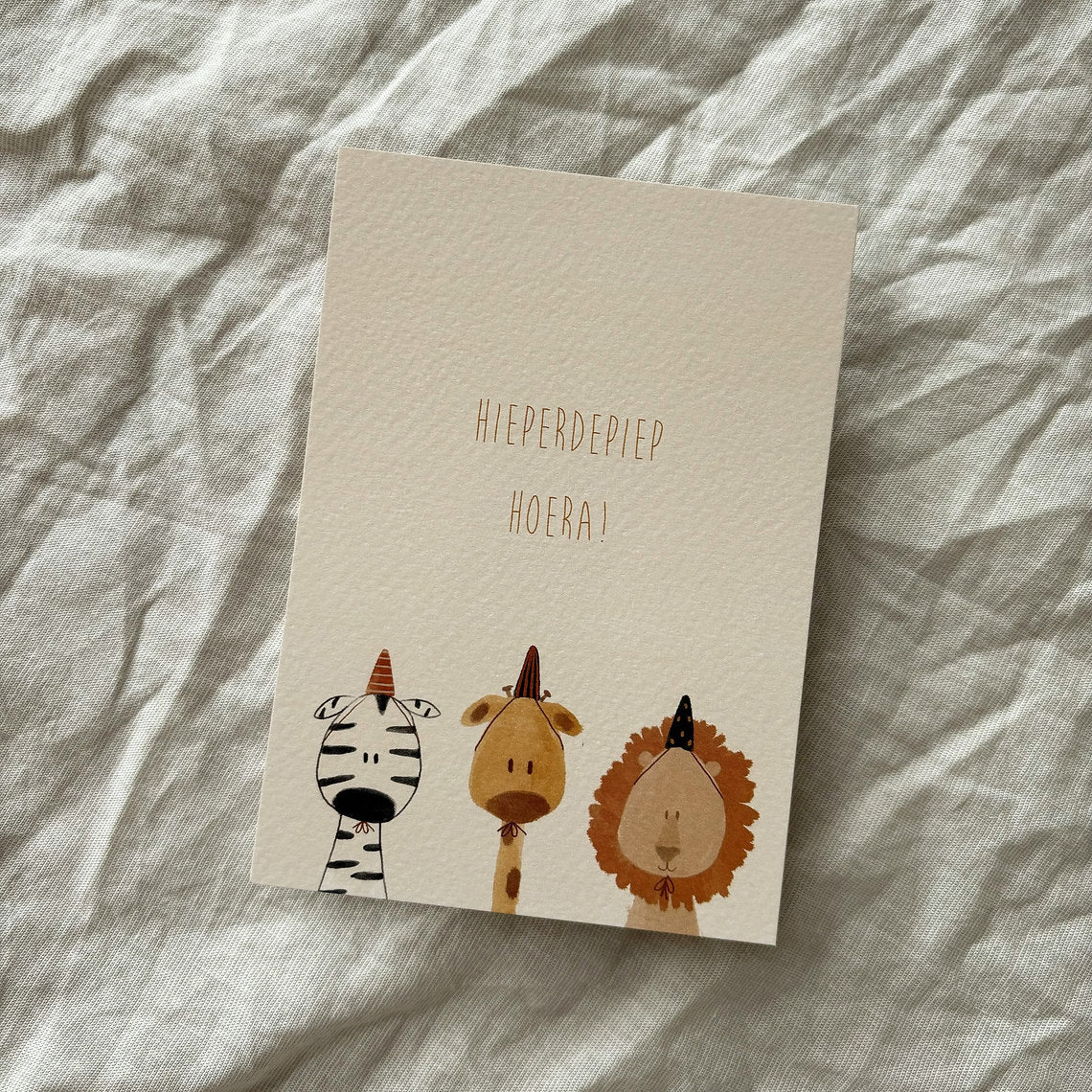 Ansichtkaart voor een verjaardag met zebra, giraffe en leeuw met feesthoedjes en tekst Hieperdepiep hoera.