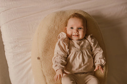 Baby ligt comfortabel op een voedingskussen met merino wollen voedingskussenhoes